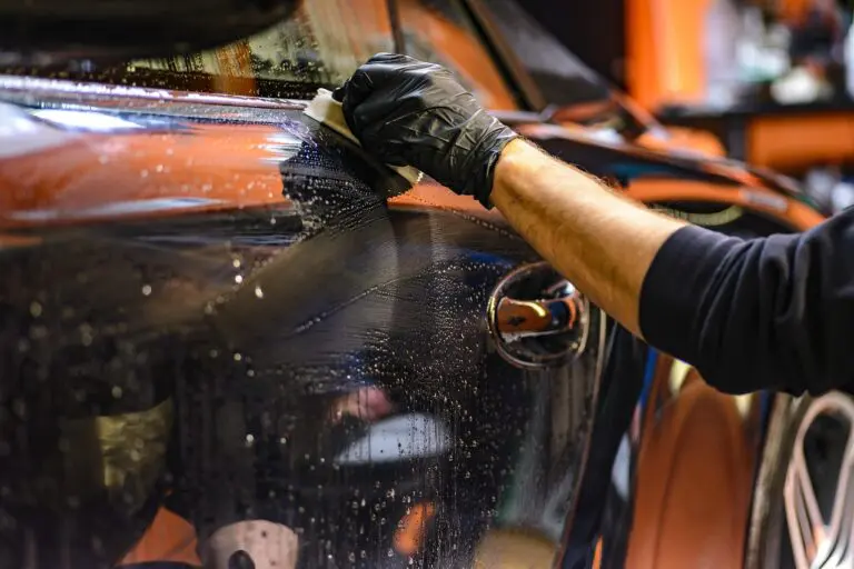 nettoyage d'une voiture orange avec un gant noir et de l'eau savonneuse