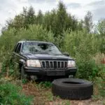 jeep abandonnée avec vitre brisée et pneu détaché dans la nature