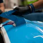 technicien appliquant un film protecteur bleu sur une carrosserie automobile