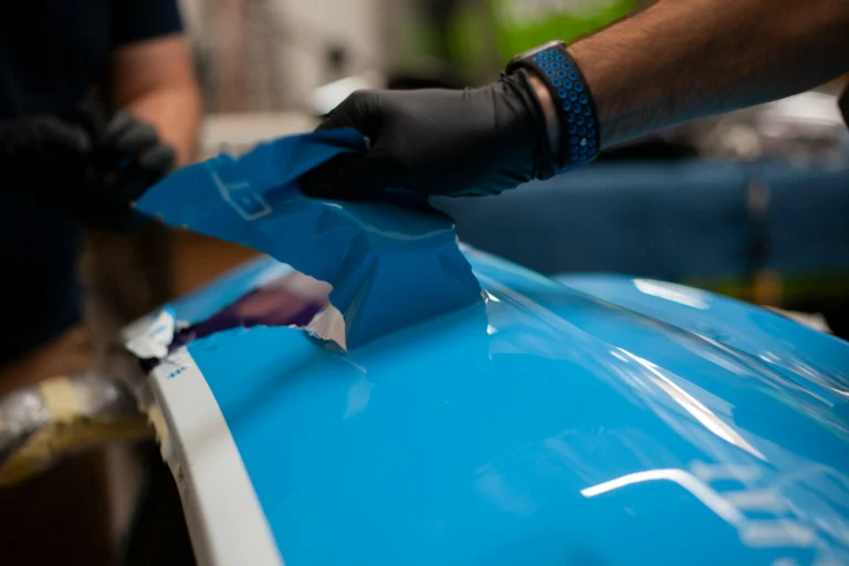 technicien appliquant un film protecteur bleu sur une carrosserie automobile