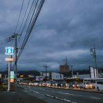 Cars lined up on a street under stormy skies.