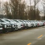 A line of brand new SUVs in an outdoor parking lot during a cloudy day.