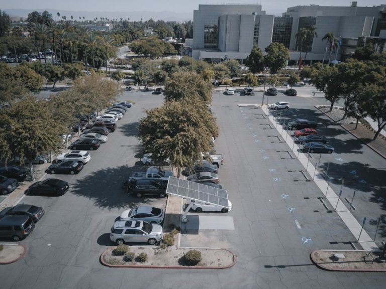 High-angle view of a parking lot with solar panels and parked vehicles, surrounded by greenery.